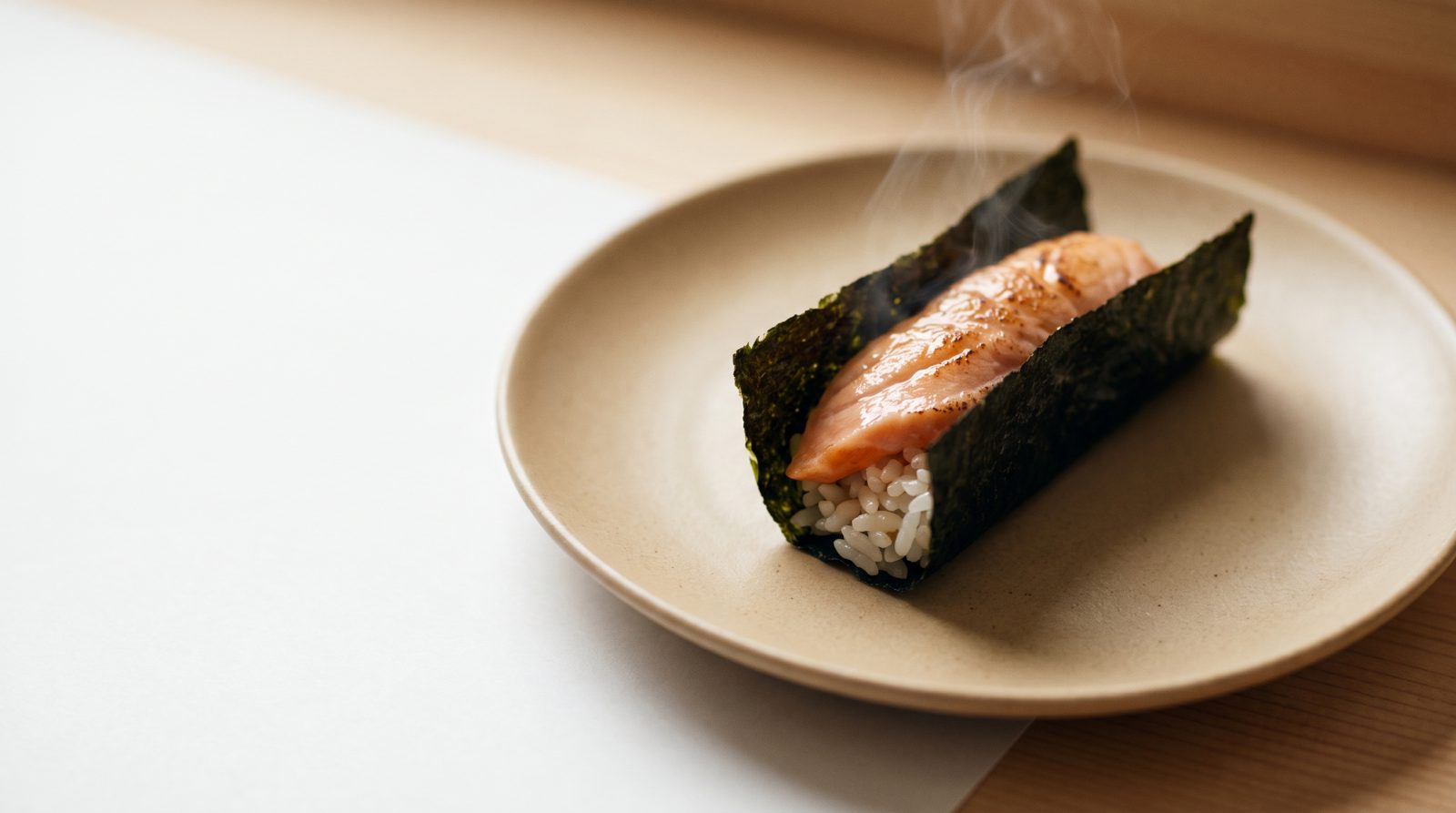 A hand-torched Hokkaido salmon handroll on warm ceramic, the nori seam running as a dark diagonal
