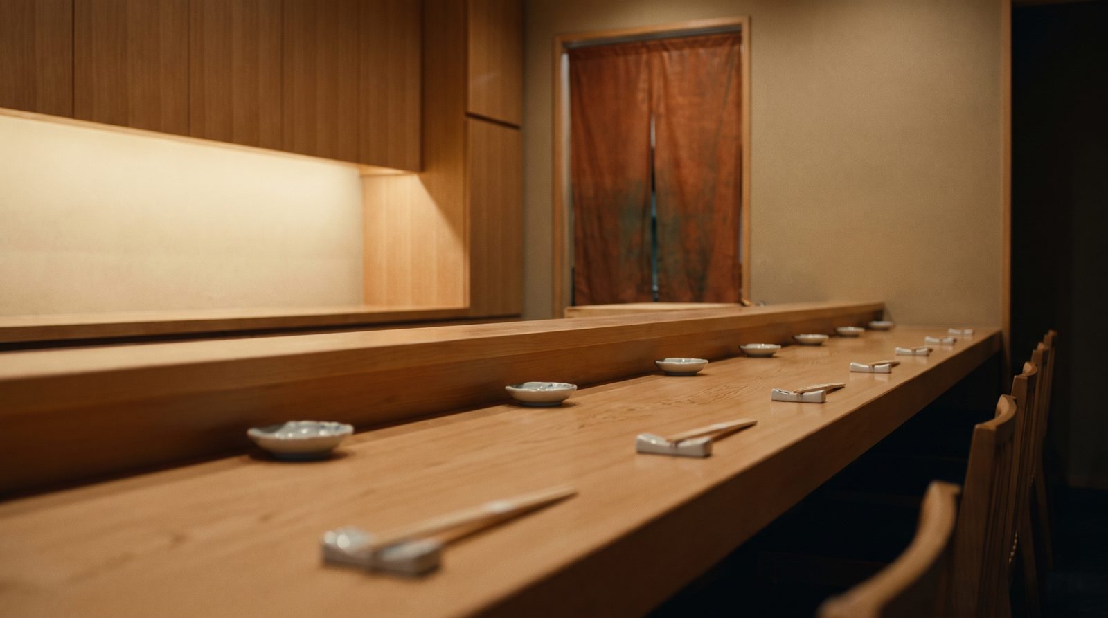A low, wide view of the ten-seat hinoki counter, lantern light pooling on pale wood